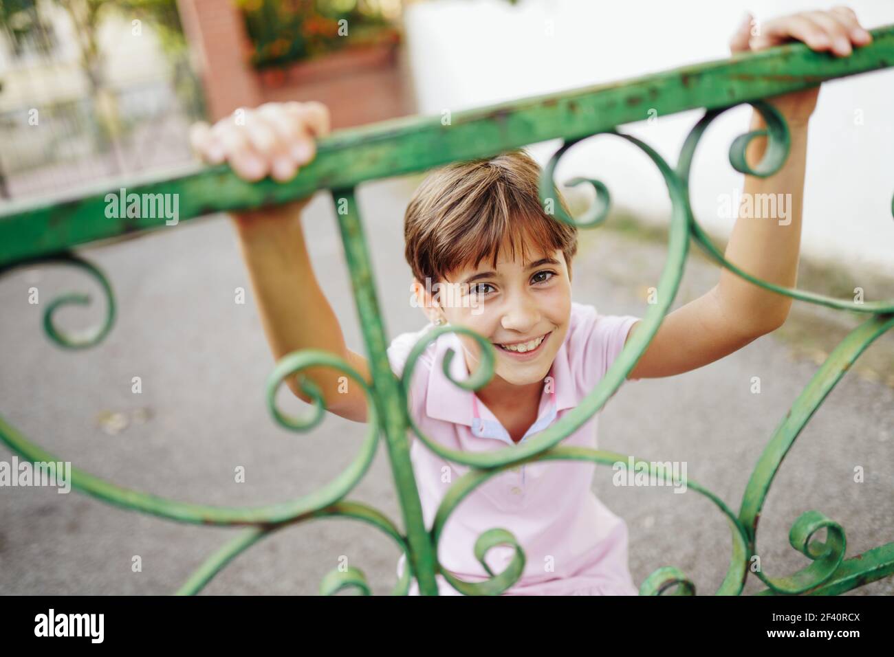 Bambina, con capelli corti, che gioca con una recinzione in ferro battuto. Bambina, otto anni, che si diverte in un parco urbano. Foto Stock