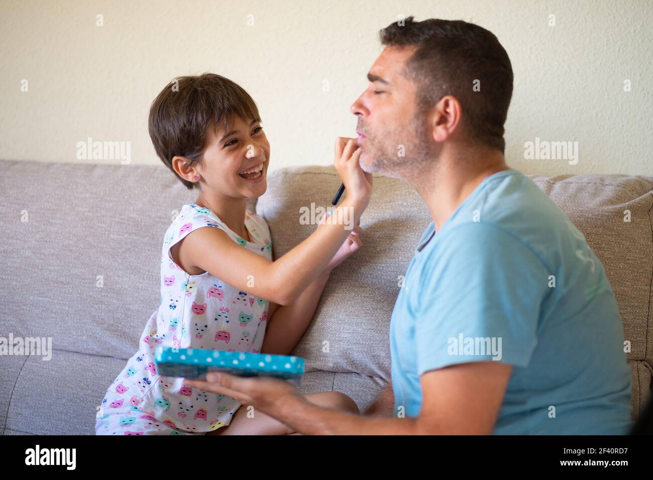 Piccola figlia carina che fa il make-up a suo padre. Papà trascorrere del tempo libero con sua figlia. Concetto di mascolinità alternativo.. Piccola figlia carina che fa il make-up a suo padre Foto Stock