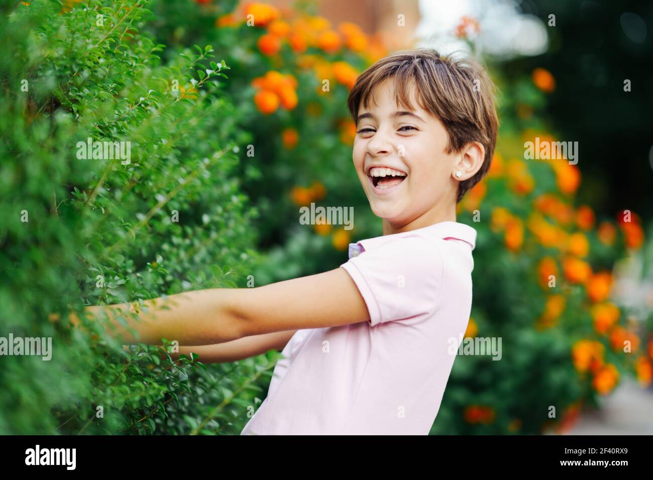 Bambina con capelli molto corti, ridendo in un parco urbano con vestito rosa. Bambina, otto anni, che si diverte in un parco urbano. Foto Stock