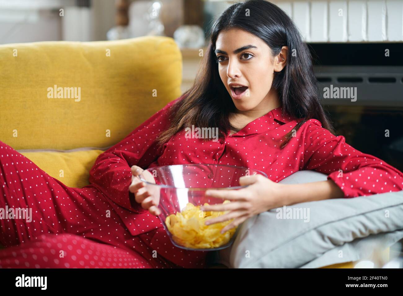 Donna persiana a casa guardando la TV. Ragazza mangiare patatine patate. Donna persiana a casa guardando la TV mangiare patate chips Foto Stock
