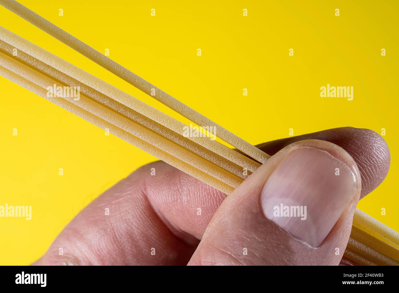 alcuni spaghetti non cotti tra le dita della mano Foto Stock