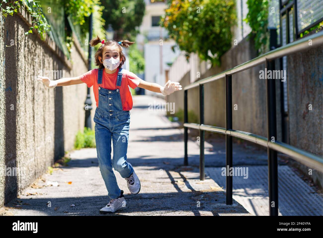 Bambina che corre all'aperto indossando una maschera di protezione contro il coronavirus durante la pandemia di Covid-19. Maschera KN95. Bambina che corre all'aperto indossando una maschera di protezione contro il coronavirus durante la pandemia di Covid-19 Foto Stock