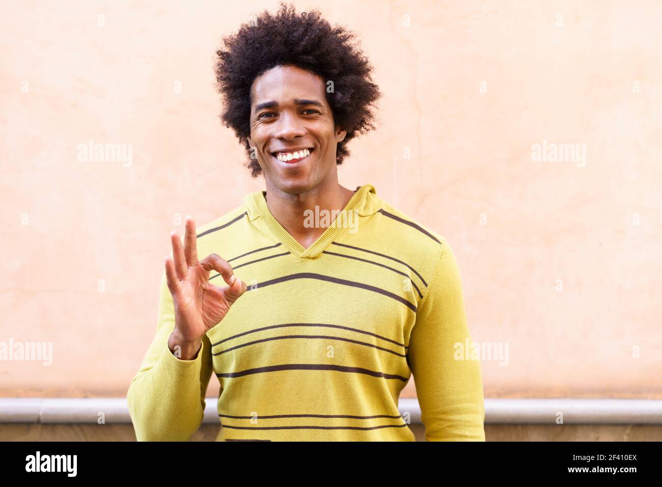 Uomo nero con capelli afro che mette un'espressione divertente all'aperto. OK gesto con la mano. Uomo nero con capelli afro che mette un'espressione divertente Foto Stock