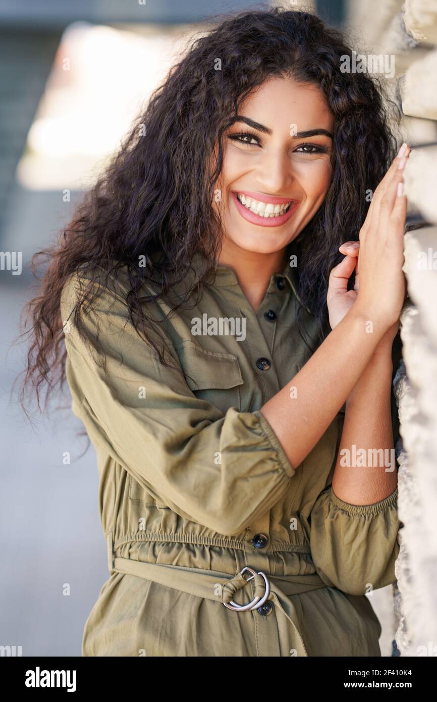 Giovane Araba Donna con capelli ricci ridendo in ambiente urbano. Donna araba felice con capelli ricci all'aperto Foto Stock