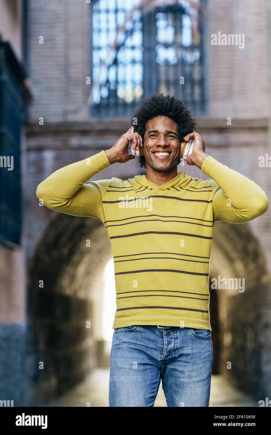 Uomo nero con capelli afro ascolto di musica con cuffie wireless visite turistiche a Granada, Andalusia, Spagna.. Uomo nero che ascolta la musica con le cuffie wireless per visitare Granada Foto Stock