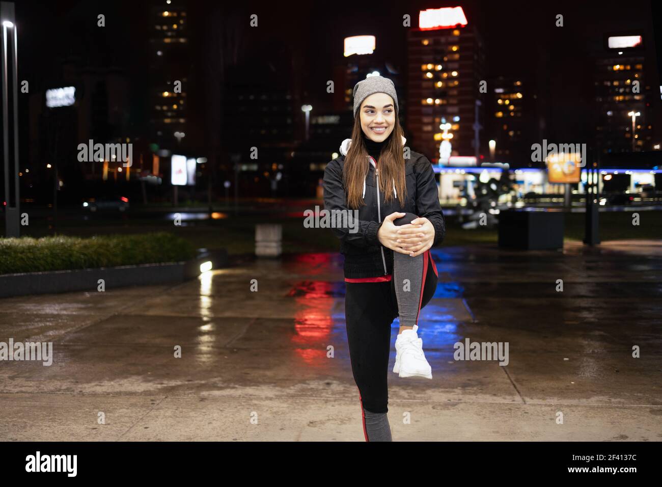 Giovane donna che allunga le gambe come un pre-workout e godendosi una bella serata piovosa in una grande città Foto Stock