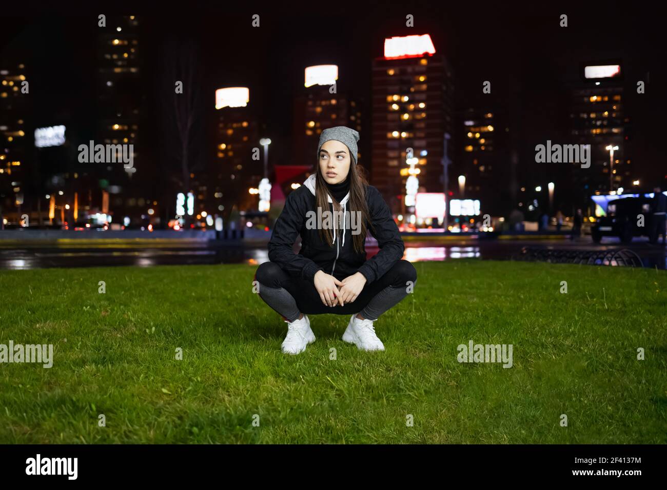 Giovane donna squatting mentre si prepara per l'allenamento notturno all'aperto in una grande città Foto Stock