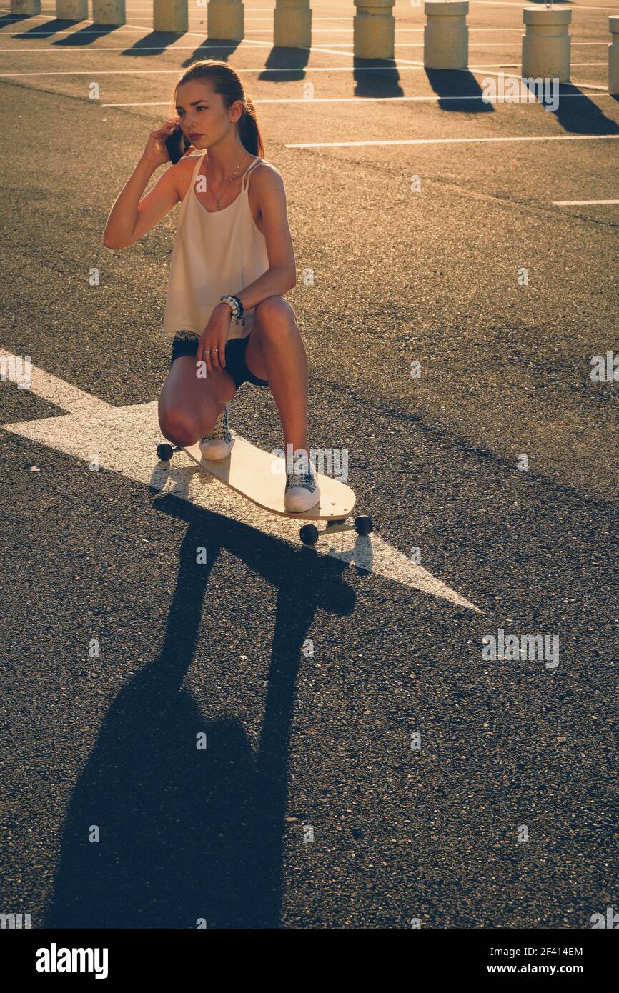 Donna sullo skateboard che parla al telefono in una giornata di sole nello skate Park. Donna sullo skateboard che parla al telefono in giornata di sole Foto Stock