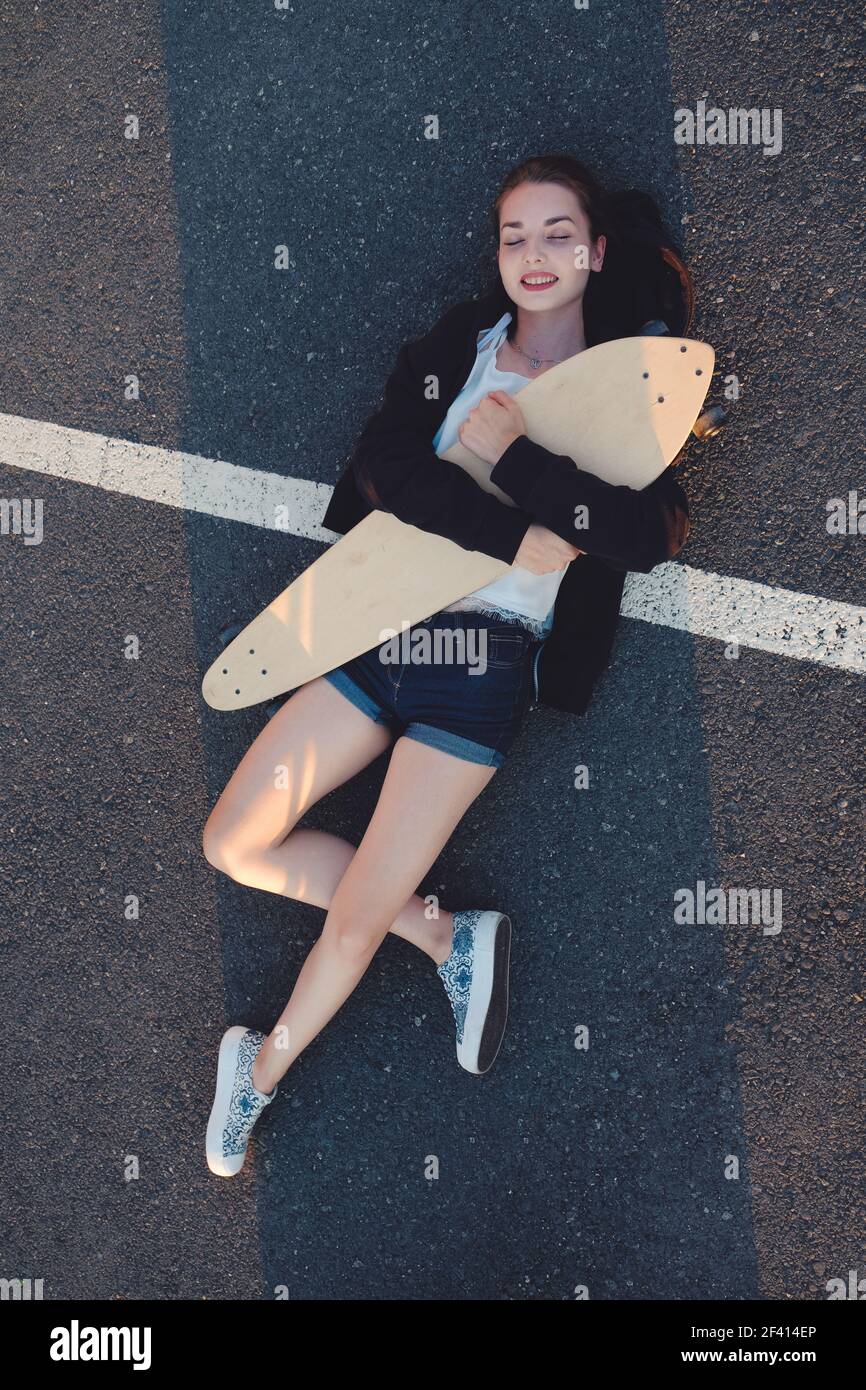 Skateg ragazza sdraiata con il suo longboard su asfalto strada superficie sopra la vista. Skateg ragazza sdraiata con il suo longboard su asfalto strada superficie Foto Stock