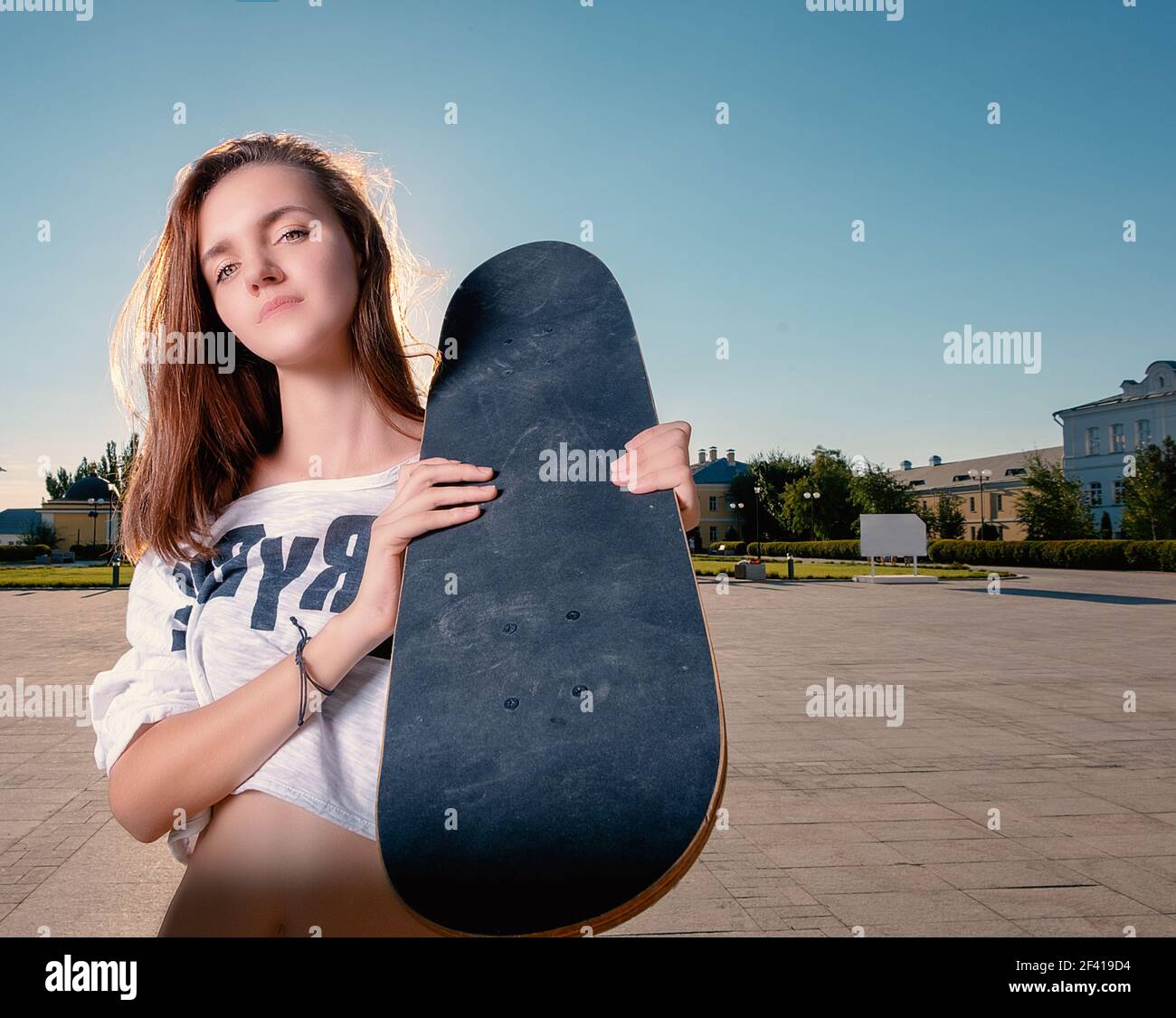 Ampio angolo di tiro della ragazza skater con skateboard sul suo grido, un sacco di spazio per il testo sul cielo. Un'ampia inquadratura di skater girl con skateboard sul suo grillatore Foto Stock