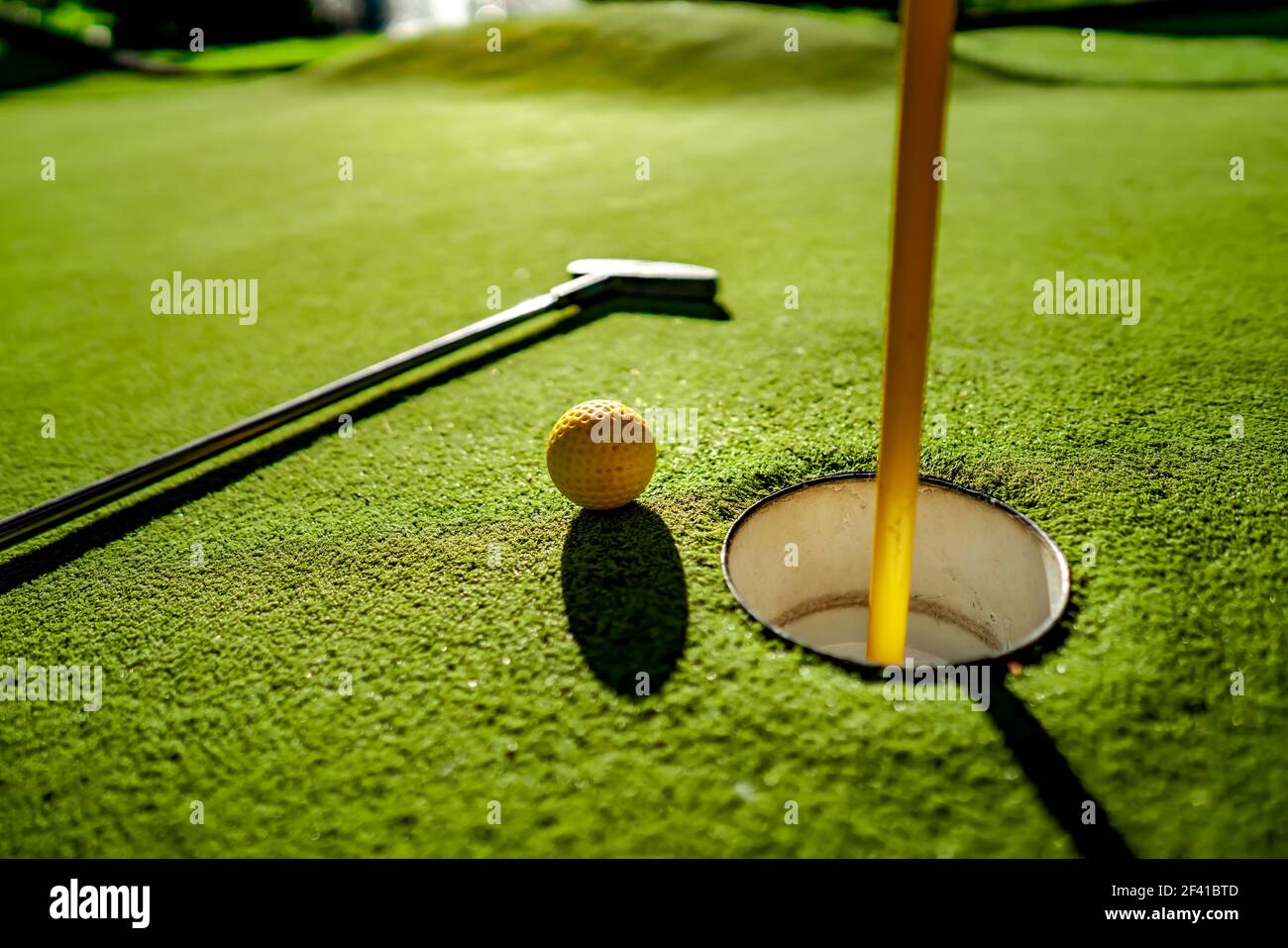 Mini Golf sfera gialla con un bat in prossimità del foro al tramonto Foto Stock