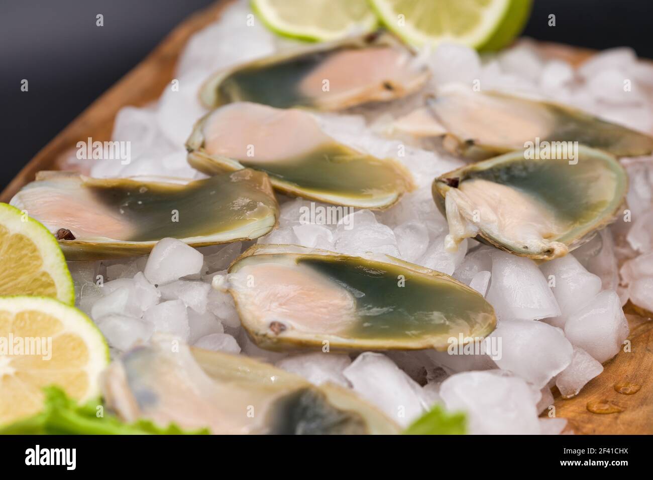 Conchiglia fresca cruda (macha), presentata su tavola di legno con ghiaccio tritato. Foto Stock