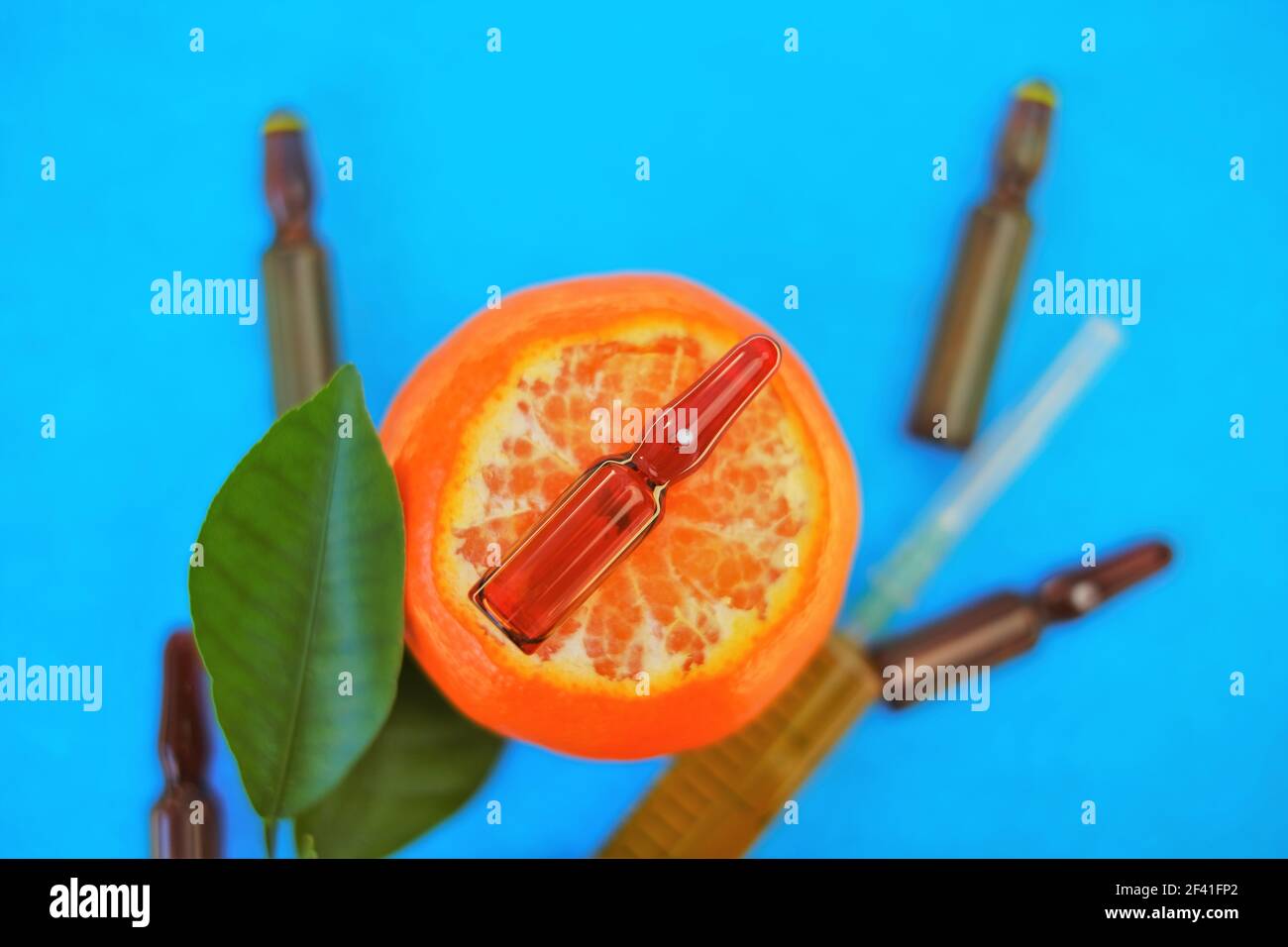 Siero di vitamina C. con vitamina C. fiale di vetro e siringa con soluzione iniettabile su mandarino frutti con foglie di colore verde brillante su blu brillante Foto Stock