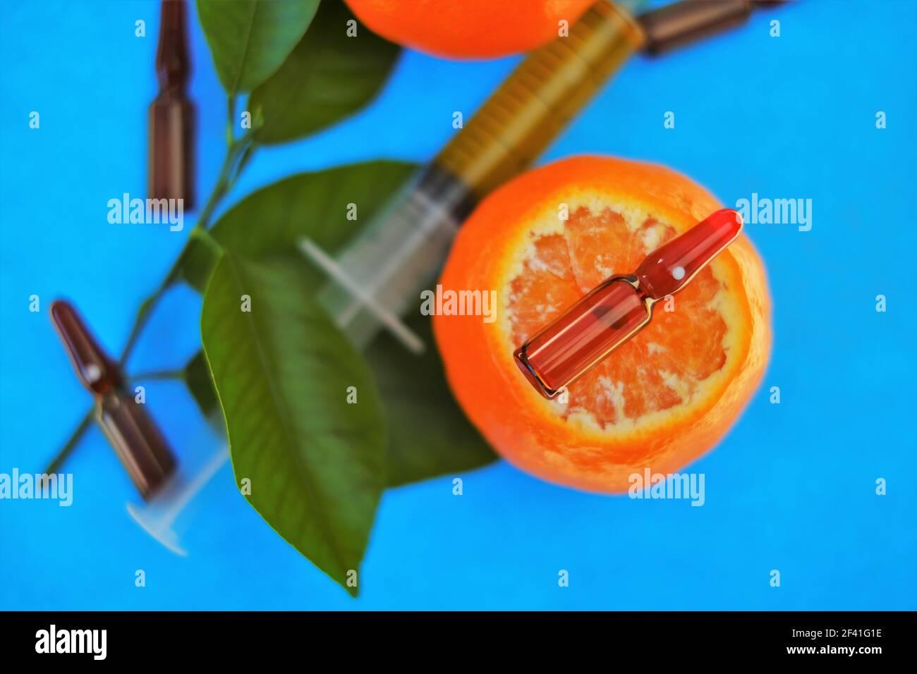 Siero di vitamina C. con vitamina C. ampolle di vetro da vicino e siringa con soluzione iniettabile su mandarino frutti con foglie verdi su blu brillante Foto Stock
