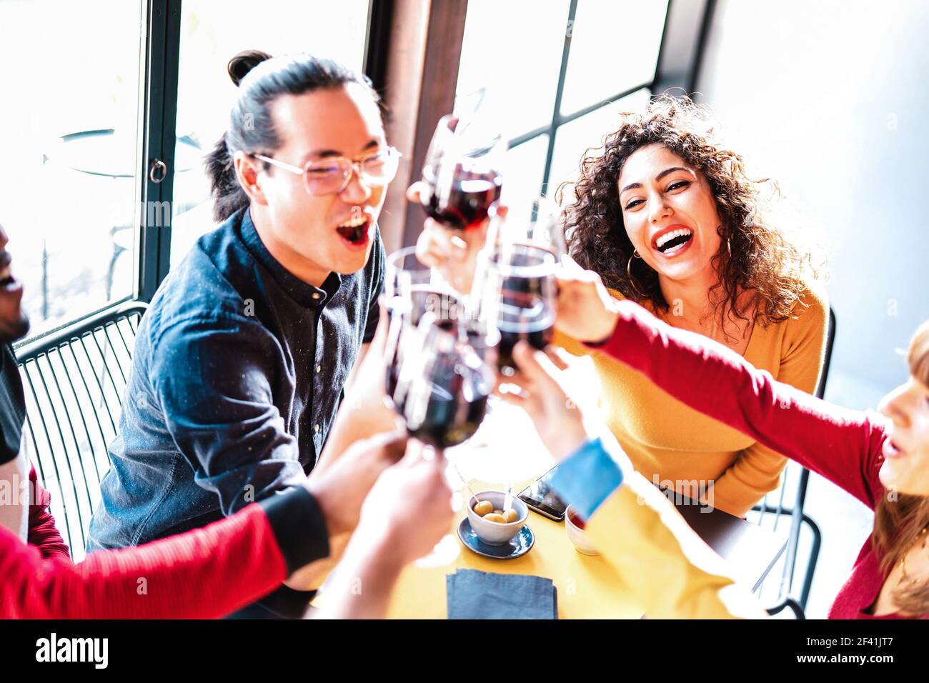 Giovani amici multirazziali che bevono e tostano vino rosso a cena Festa - gente ubriaca felice che si diverte insieme al ristorante cantina bar Foto Stock