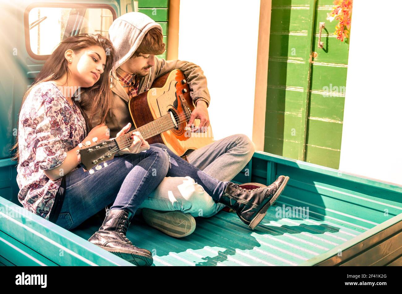 Giovane coppia romantica di amanti che suonano la chitarra all'aperto con il sole dopo la pioggia Foto Stock