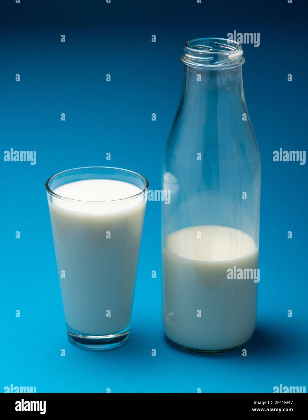 Bicchiere di latte fresco e bottiglia di latte isolato su fondo blu. Foto Stock