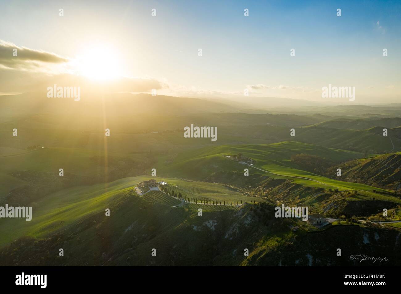 Vista aerea delle colline verdeggianti e della scintillante luce del sole in Italia, con una piantagione e una piccola fattoria in cima Foto Stock