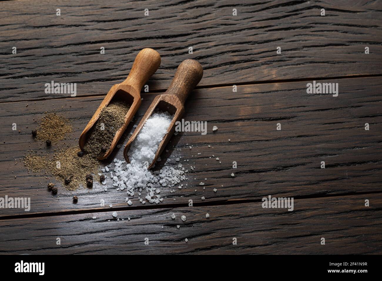 Sale di mare e pepe macinato in cucchiai di legno su vecchio sfondo di legno. Due ingredienti più popolari che si mettono in cibo. Foto Stock