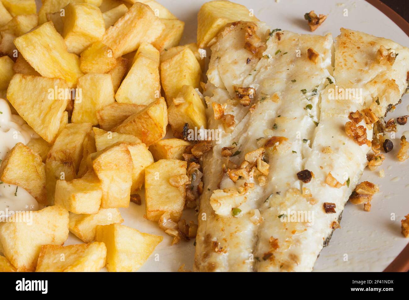 Filetto di nasello con aglio servito con patatine fritte tagliate a quadrati su un piatto da cucina. Ricette vegetariane. Foto Stock