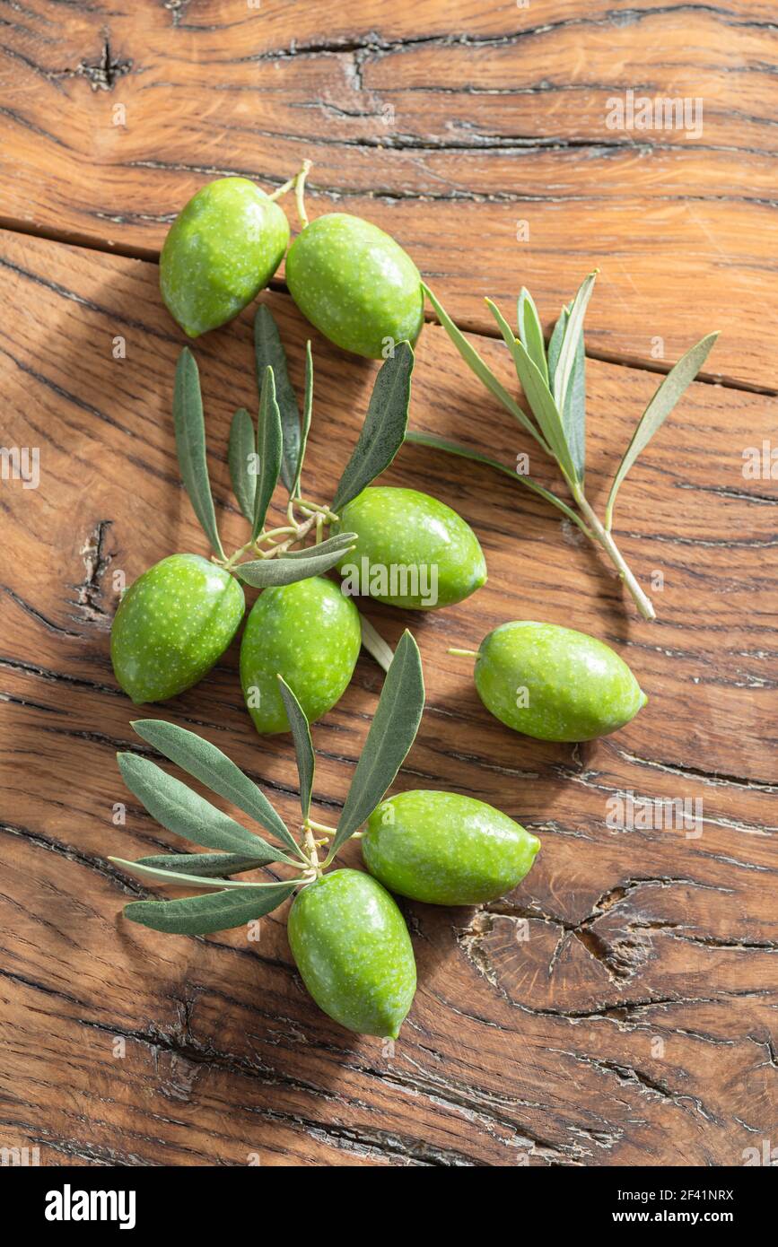 Olive verdi naturali con foglie d'oliva su un tavolo di legno d'epoca. Foto Stock