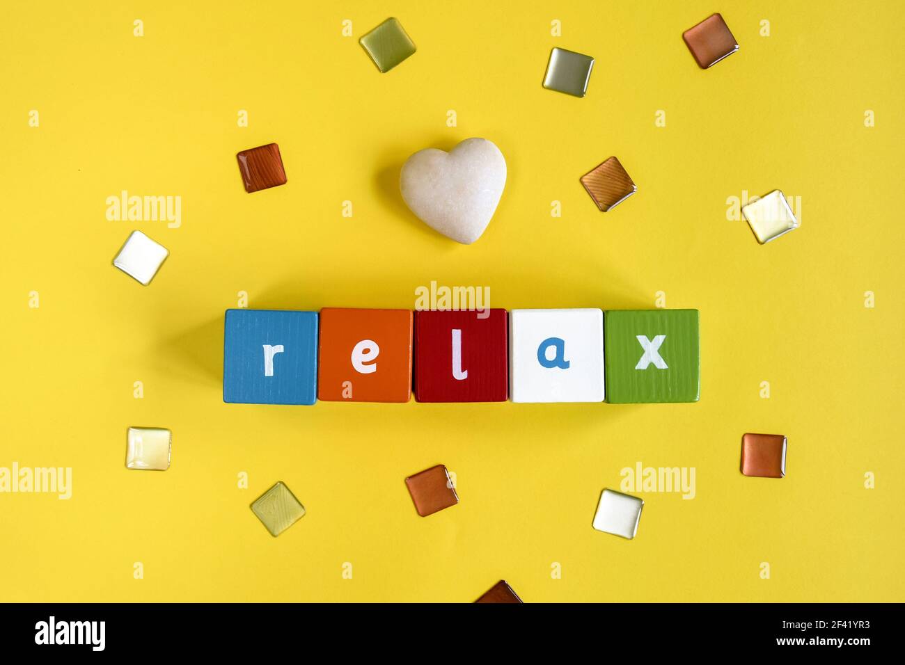 RELAX - Parola fatta da blocchi di legno colorati. Cubetti dipinti con lettere e un cuore di pietra su sfondo giallo. Vista dall'alto. Spazio di copia. Foto Stock