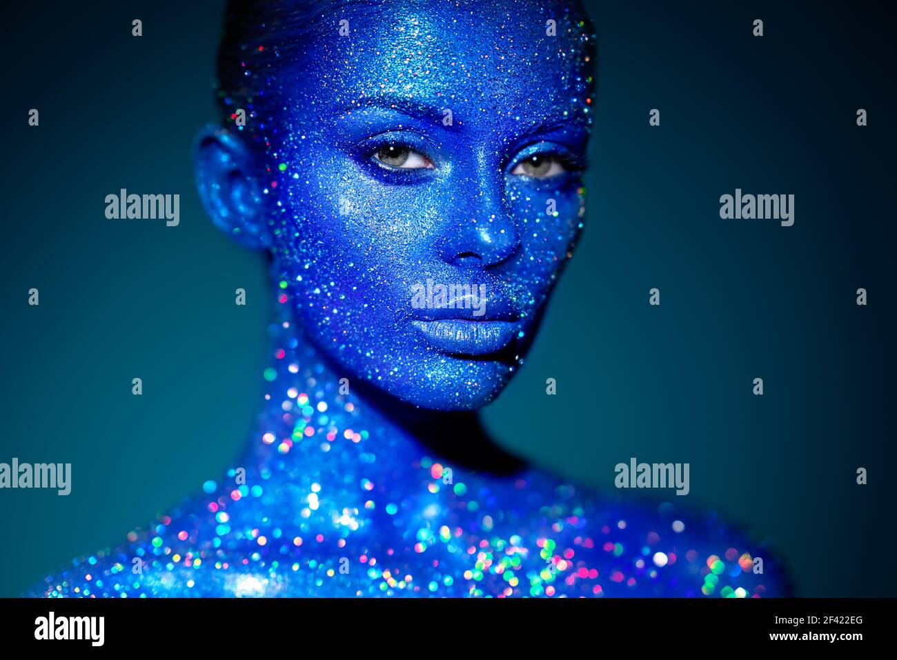 Donna modello di moda in blu scintille luminose e luci al neon in posa in studio. Ritratto di bella donna sexy. Art design colorato glitter incandescente compongono Foto Stock