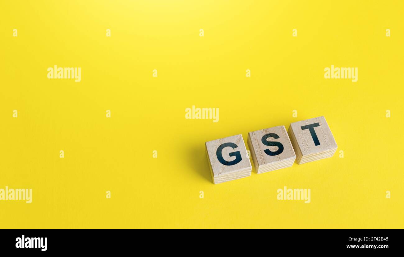 Blocchi con lettere GST (imposta sui beni e servizi) su sfondo giallo. Politica finanziaria statale volta a regolamentare le regole di riscossione delle imposte e a ridurre la burocrazia Foto Stock