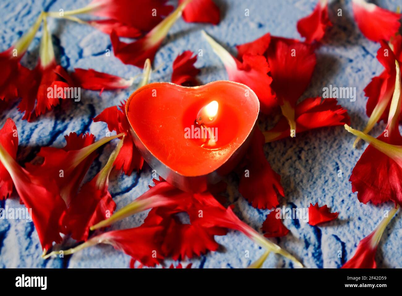 Petali rossi di garofano e una candela a forma di cuore Foto Stock