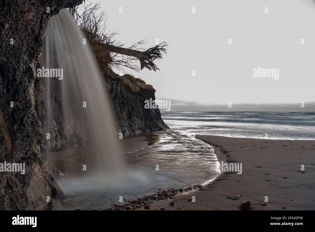 cascata del tramonto sul pavimento vicino al mare con un bella piccola estuario del fiume nelle ampie acque del mare e. nuvole all'orizzonte Foto Stock