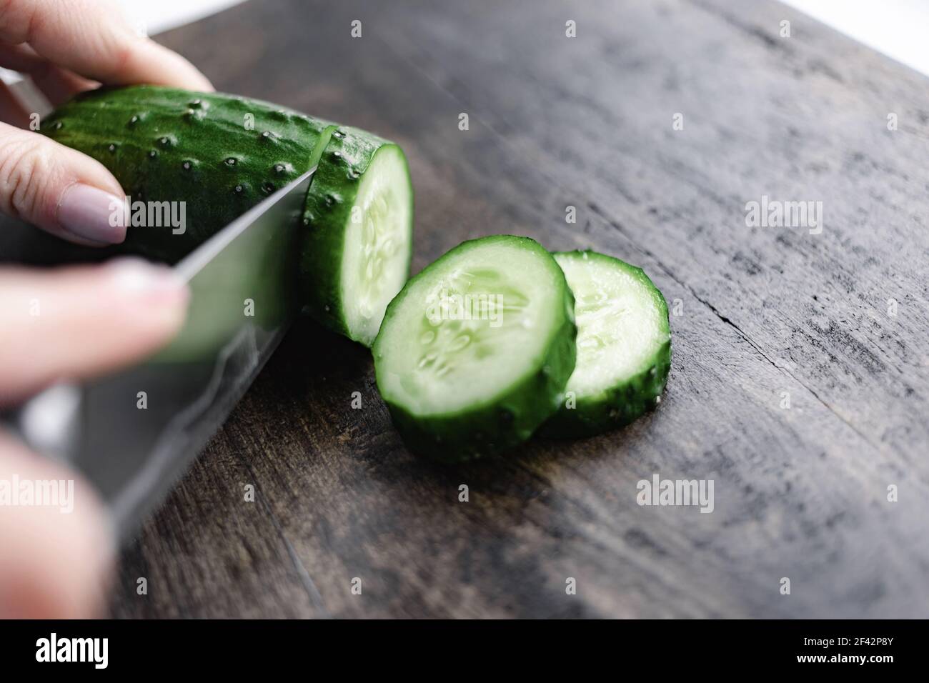 donna che taglia a mano il cetriolo sul legno da tritare Foto Stock