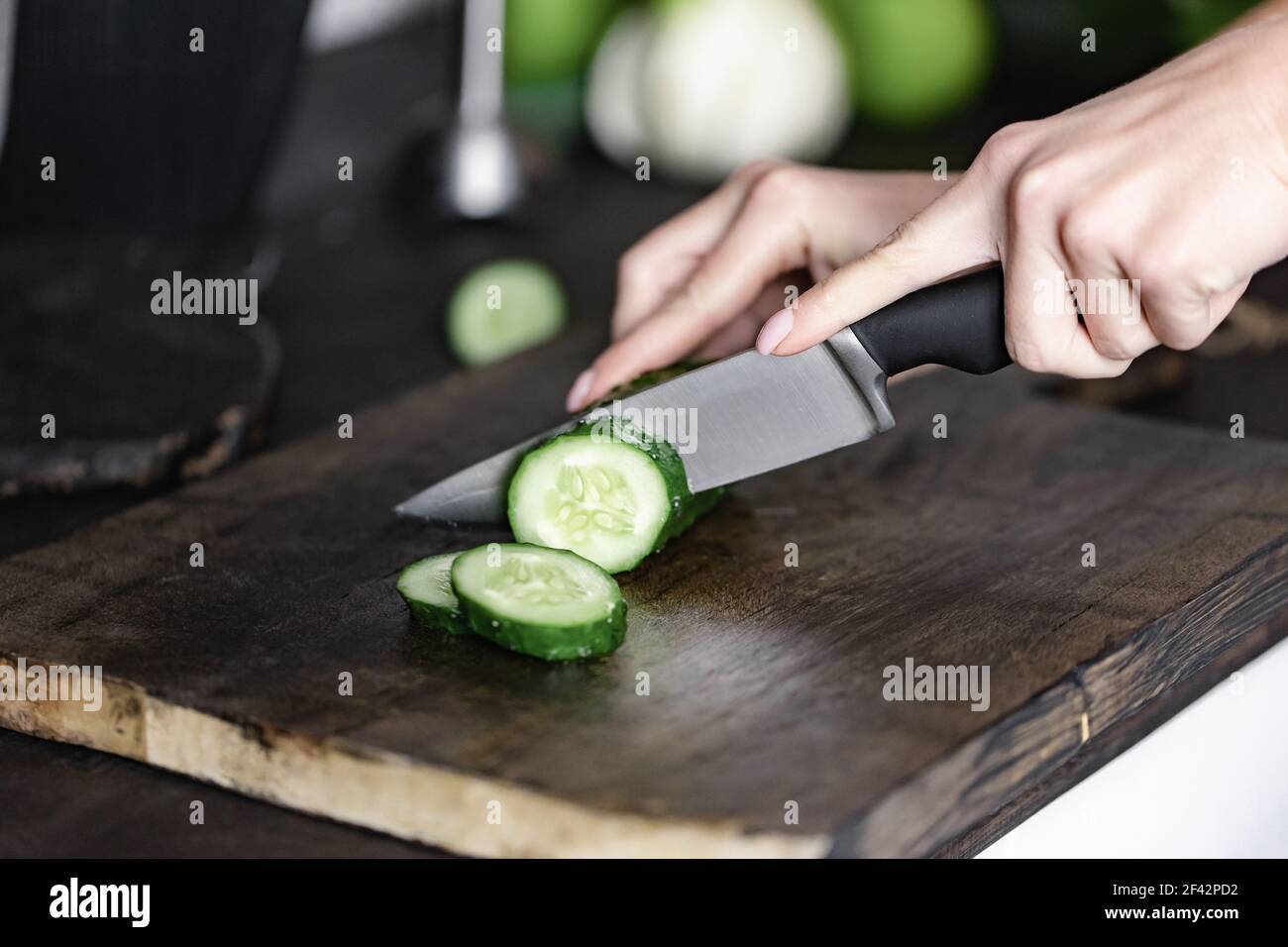 donna che taglia a mano il cetriolo sul legno da tritare Foto Stock