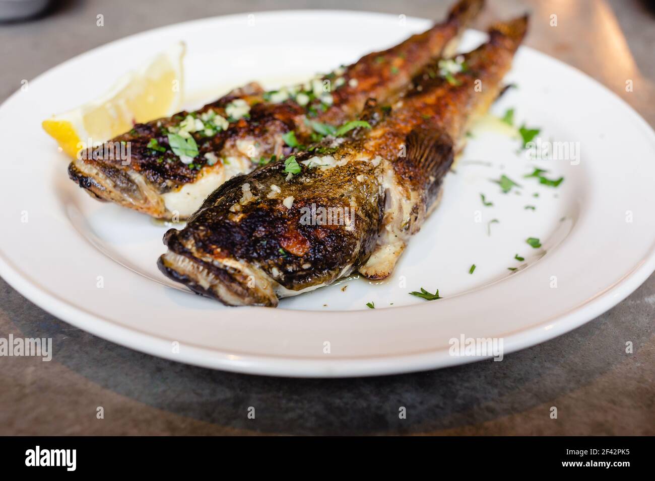 Due pesci di goda di mare fritti su piatto bianco con primo piano di limone. Cucina mediterranea, cibo spazzatura, gustosi spuntini per il concetto di birra Foto Stock