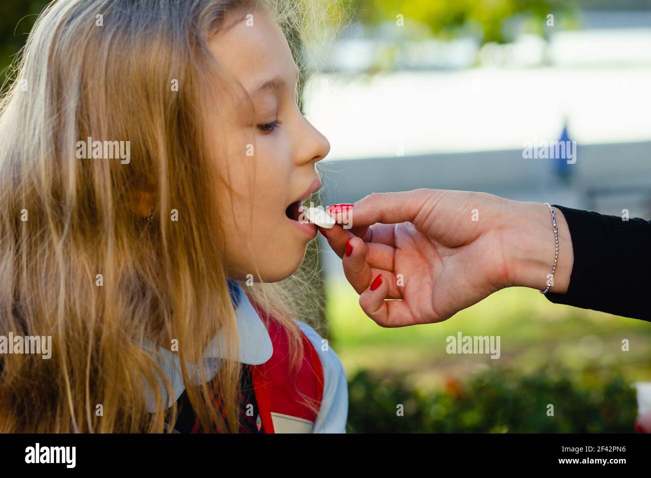 Madre giovane che dà la pillola della vitamina alla sua figlia carina piccola, all'aperto. Utile per uno sviluppo adeguato. Ipovitaminosi. Foto Stock