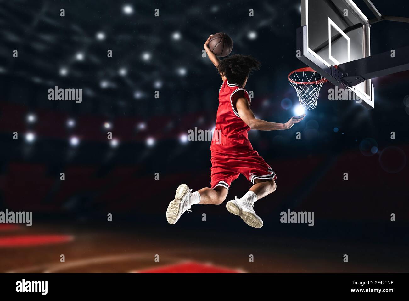 Giocatore di pallacanestro in uniforme rossa che salta in alto per fare un slam dunk al cesto Foto Stock