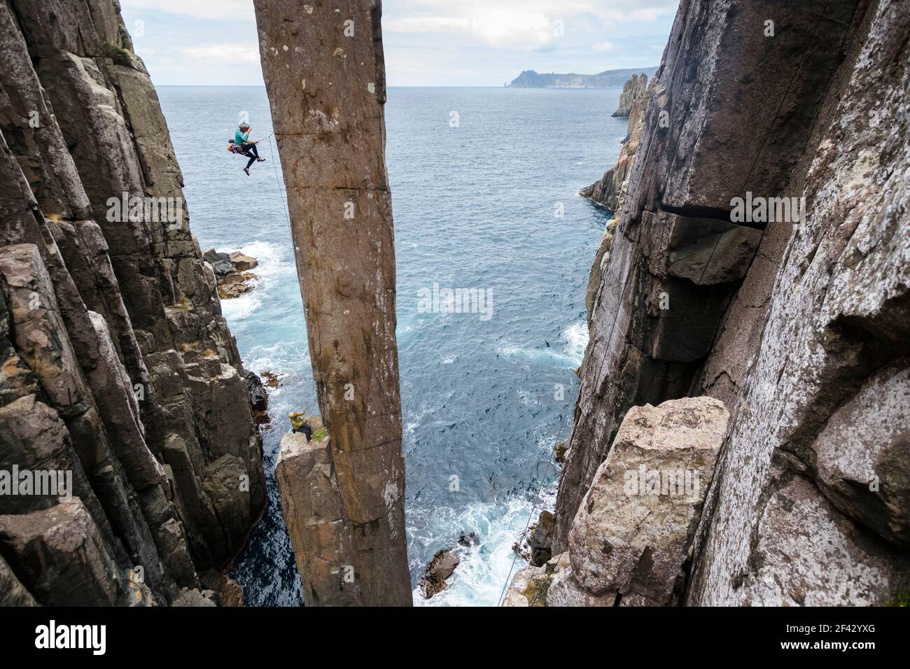 La rockclimber femminile cade mentre cerca di salire il Totem Pole, uno stack marino esposto che sorge fuori dall'oceano a Capo Hauy, Tasman National Park, Tasmania, Australia. Foto Stock