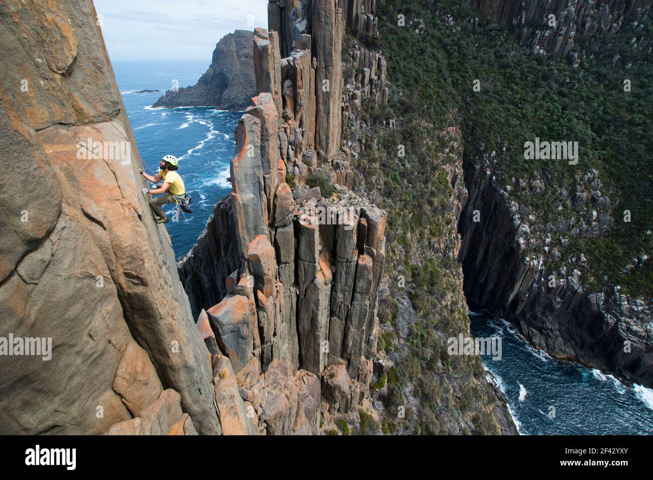 Il giovane uomo sale il bordo esposto di una cresta rocciosa di colonne lungo le scogliere del mare che emergono dall'oceano a Capo Raoul, Tasmania, Australia. Foto Stock