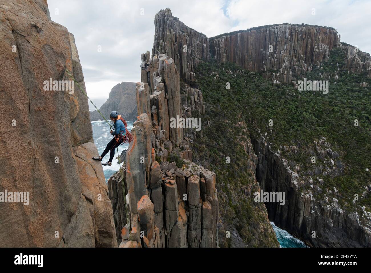 Il rockclimber femminile guarda giù mentre usa una corda per rappel dal bordo di una scogliera di mare per continuare ad esplorare le colonne dolerite di Capo Raoul, Tasmania, Australia. Foto Stock