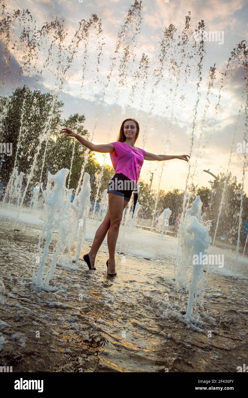 Dnepropetrovsk, Ucraina - 08.20.2017: Gioiosi cittadini ballano sulla piazza della città al tramonto. Giovane bella ragazza che balla sotto la fontana. Foto Stock