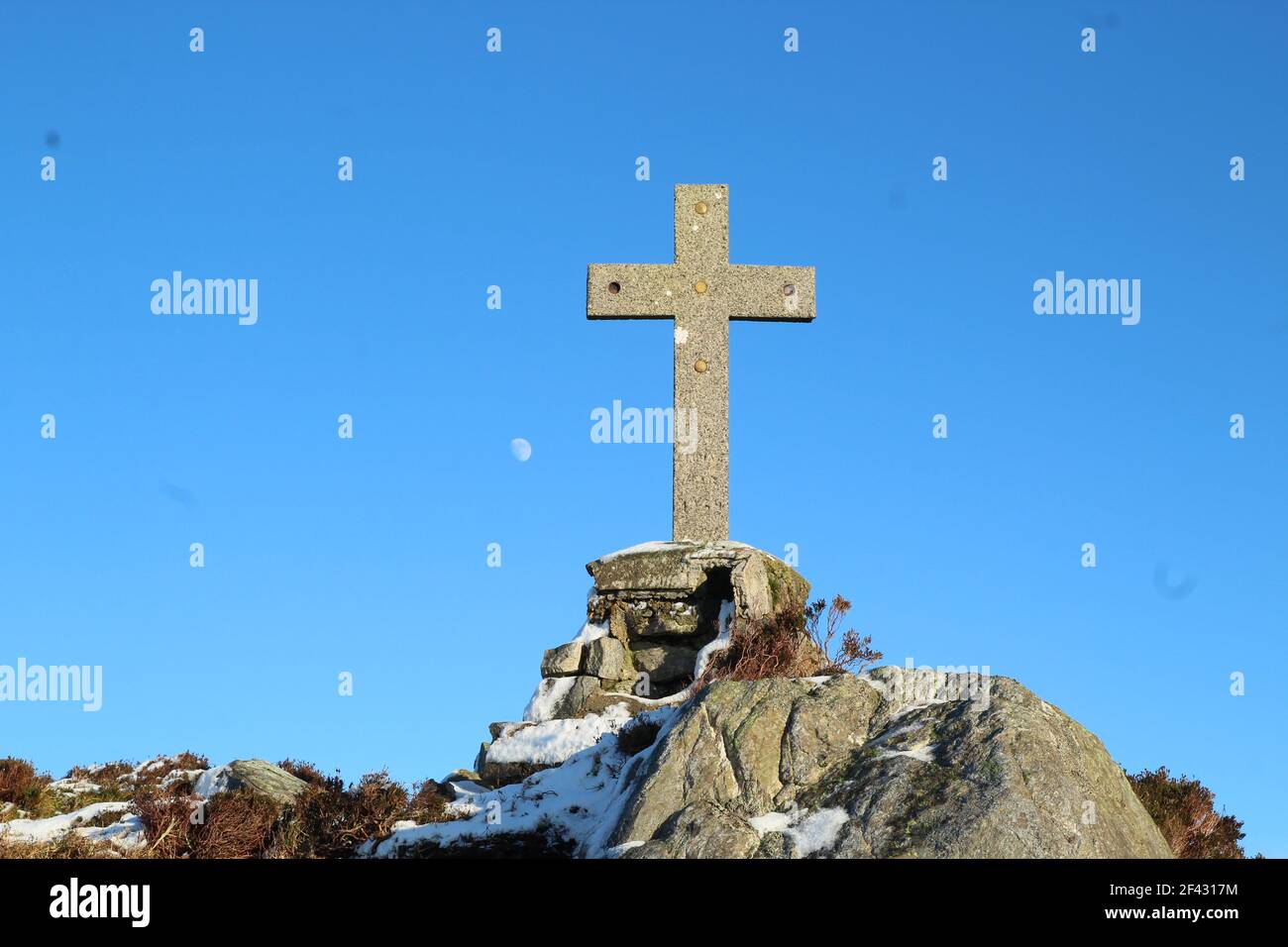 Croce scolpita da pietra in cima alla roccia sulla collina contro lo sfondo di cielo blu con luna visibile. Contea di Leitrim, Irlanda Foto Stock
