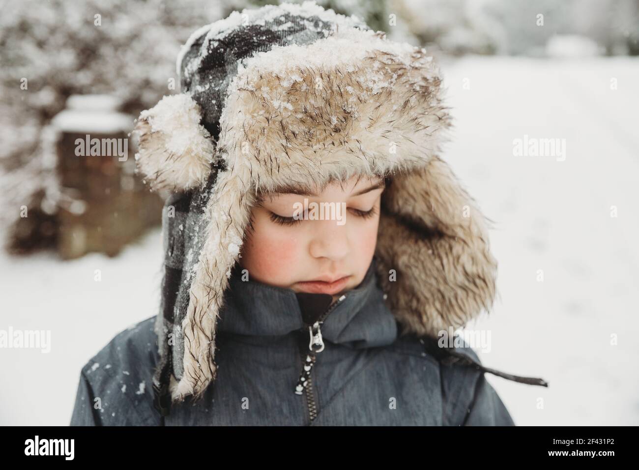 Ritratto di ragazzo che guarda giù indossando cappello di furry nella neve Foto Stock