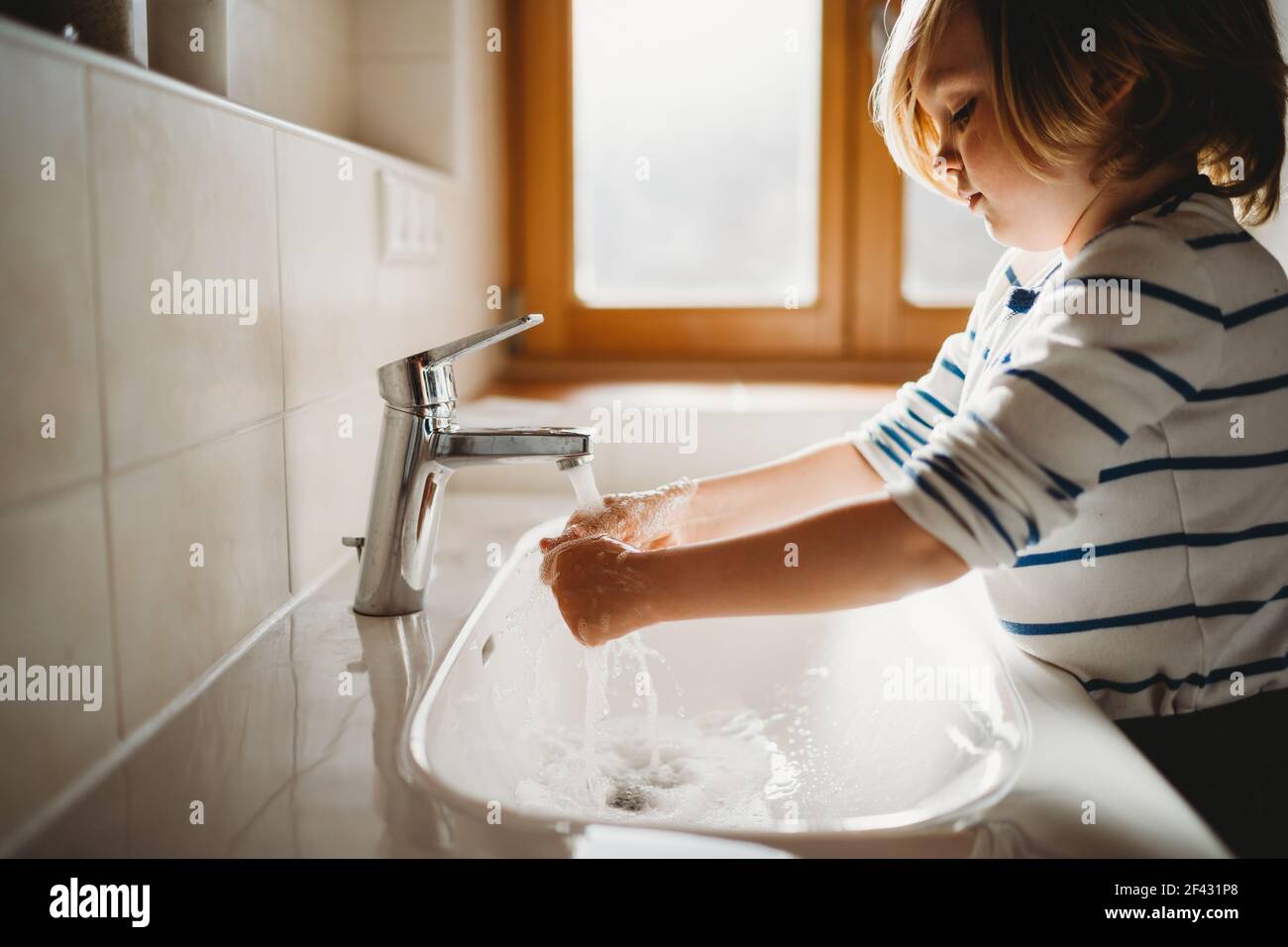 Vista laterale di bambino giovane età prescolare che lavano le mani con sapone Foto Stock