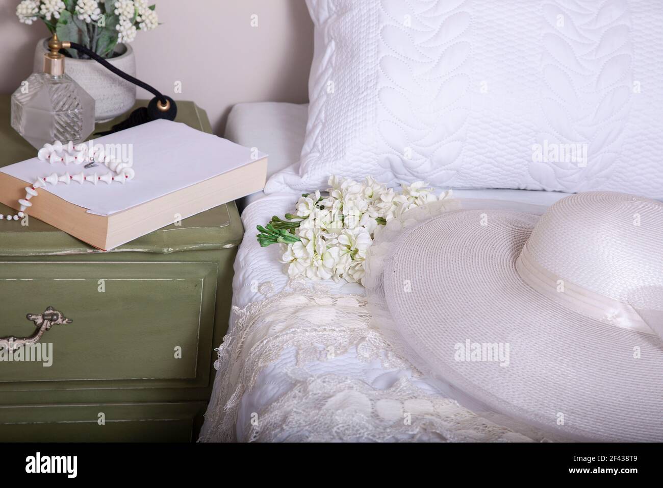 Camera da letto romantica con cappello bianco sul letto e libro su un tavolo laterale e una Domenica mattina o di preparazione per un concetto di evento. Foto Stock