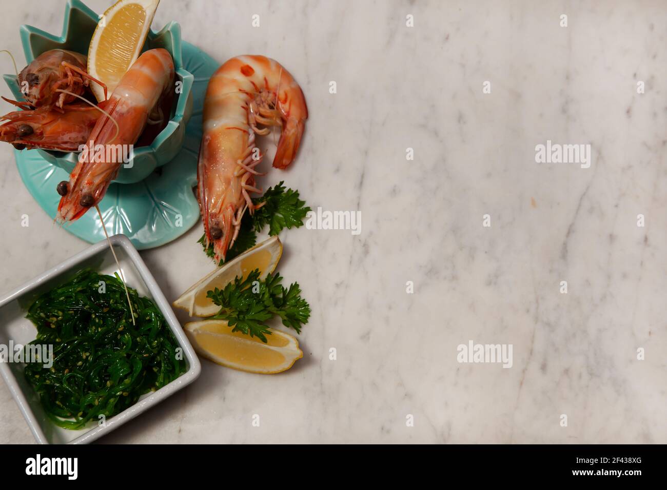Una festa di pesce con grandi gamberi del re in una ciotola verde e insalata di alghe su uno sfondo di marmo bianco e grigio con spazio di copia. Foto Stock