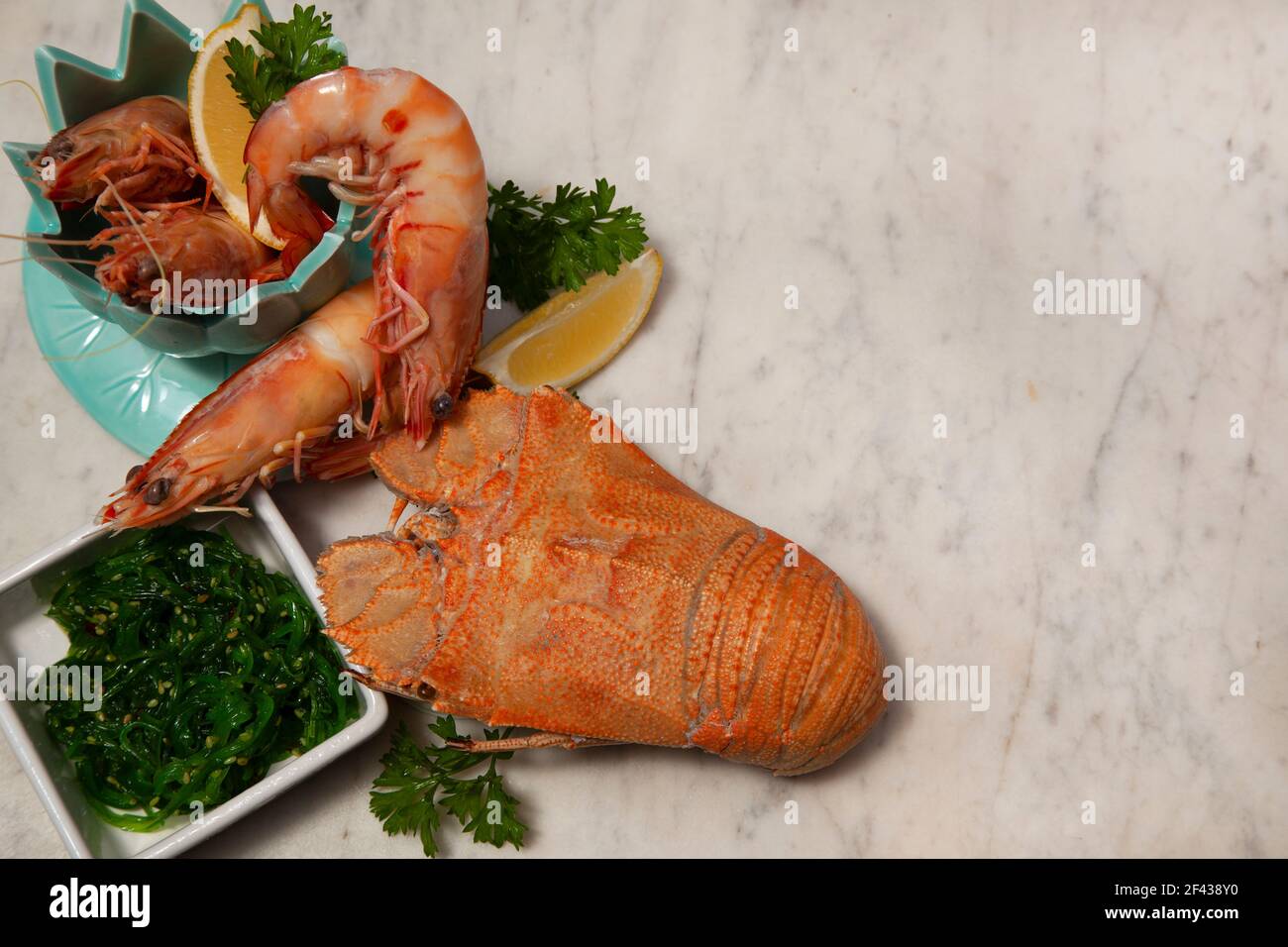 Una festa di pesce che include grandi gamberi del re in una ciotola, Moreton Bay Bug, un tipo di aragosta, e insalata di alghe su uno sfondo di marmo bianco e grigio. Foto Stock