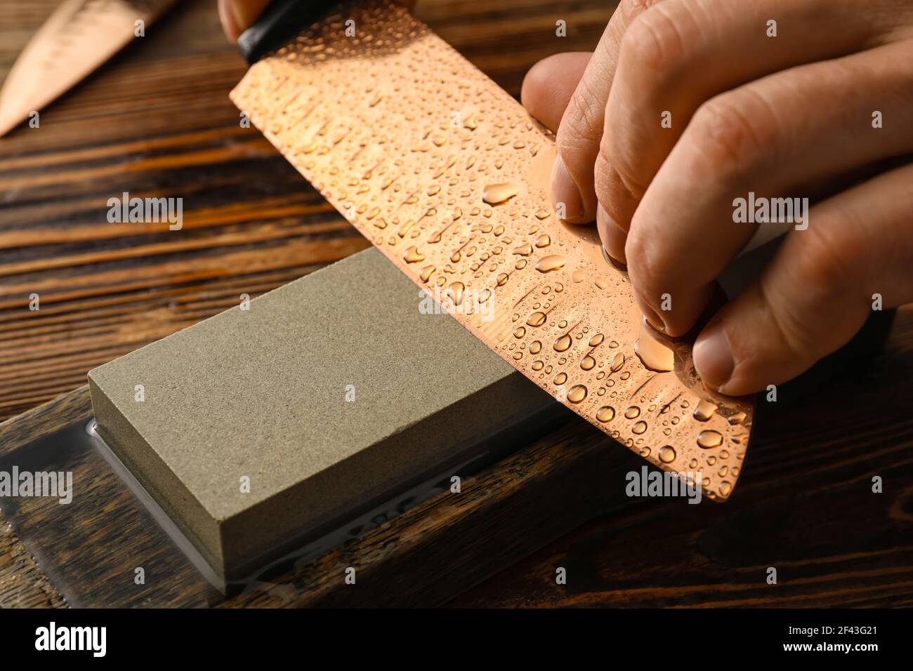 Uomo affilatura coltello su fondo di legno, primo piano Foto Stock