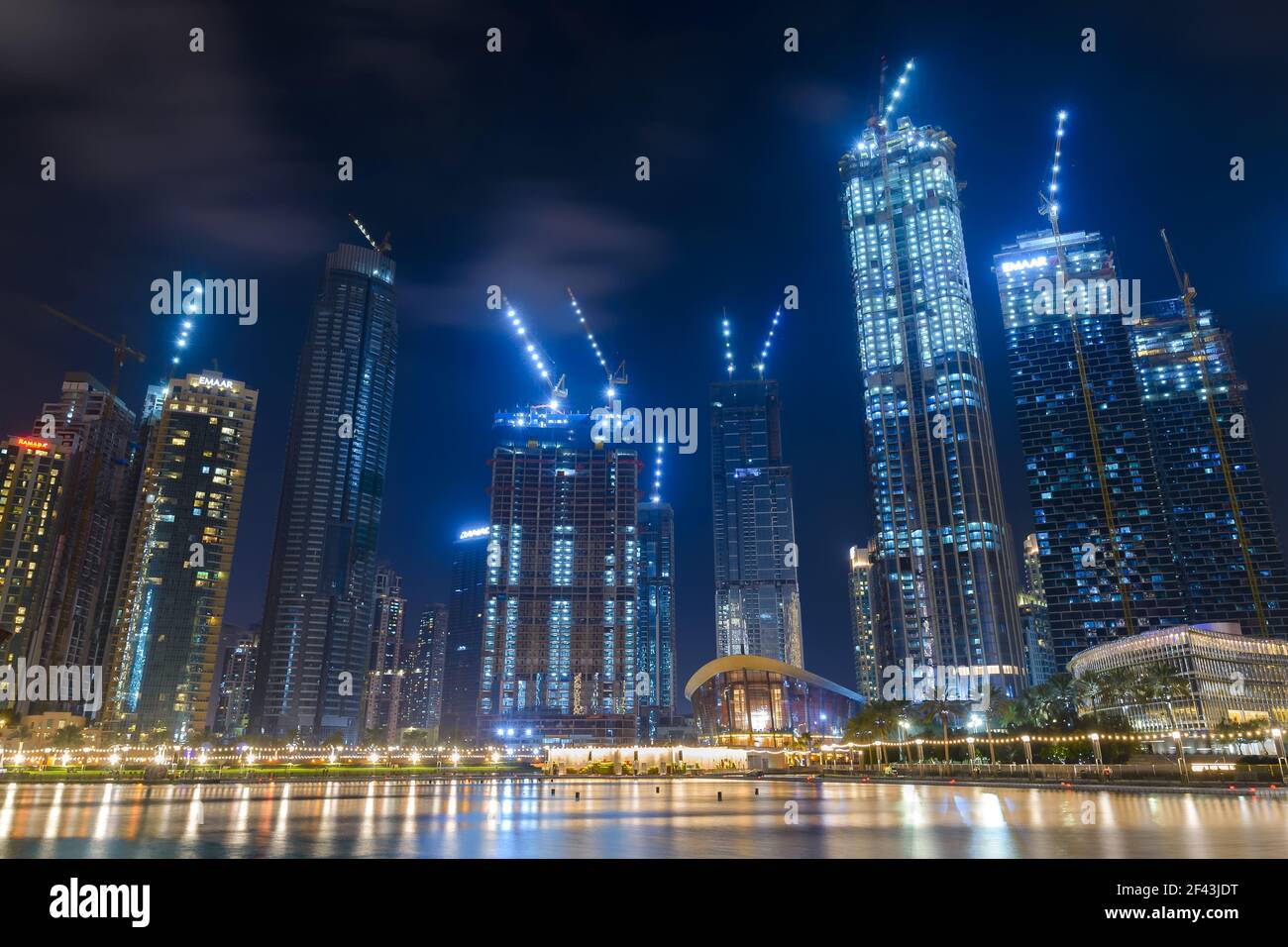 Edifici multipli con gru di notte vicino al Dubai Mall negli Emirati Arabi Uniti. Gru da costruzione illuminate. Foto Stock