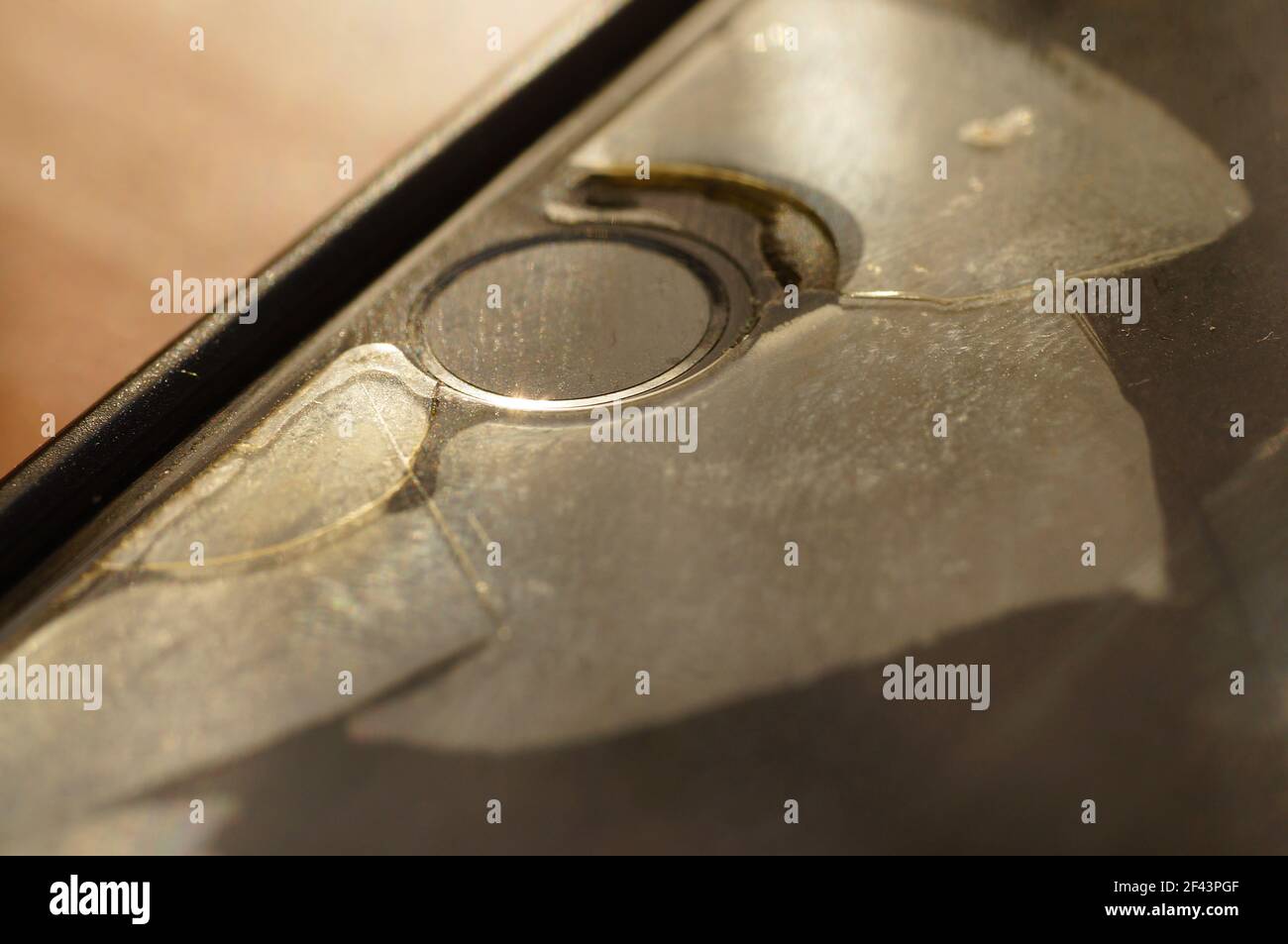 Vetro protettivo dello smartphone - danneggiato, incrinato, usurato. Vecchia protezione dello schermo. Pulsante id telefono sporco, nero, usurato. Foto Stock