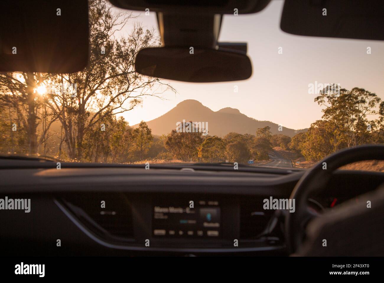 Guida attraverso la macchia di campagna australiana con montagne davanti e luce del sole dorata Foto Stock