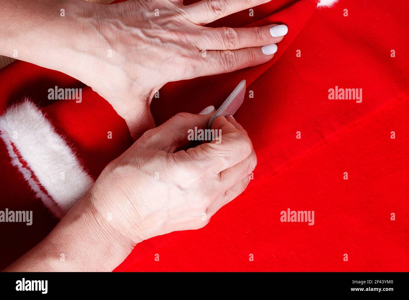 Nonna cucire piccolo cappello di Santa per i nipoti. Primo piano. Gesso del sarto nelle mani per fare il modello di cucitura. Preparazione per la Fiera di Natale della scuola. Foto Stock